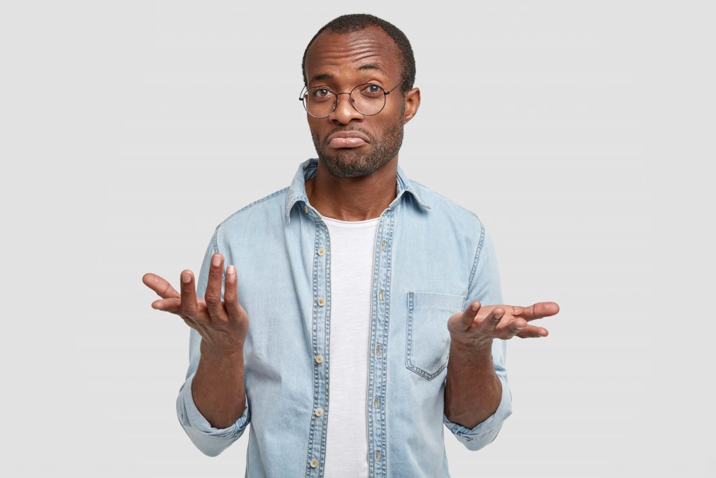 Puzzled dark skinned male look with clueless expression, looks doubtfully, can`t make decision, dressed in casual clothes, isolated over white background. People, hesitation and puzzlement concept